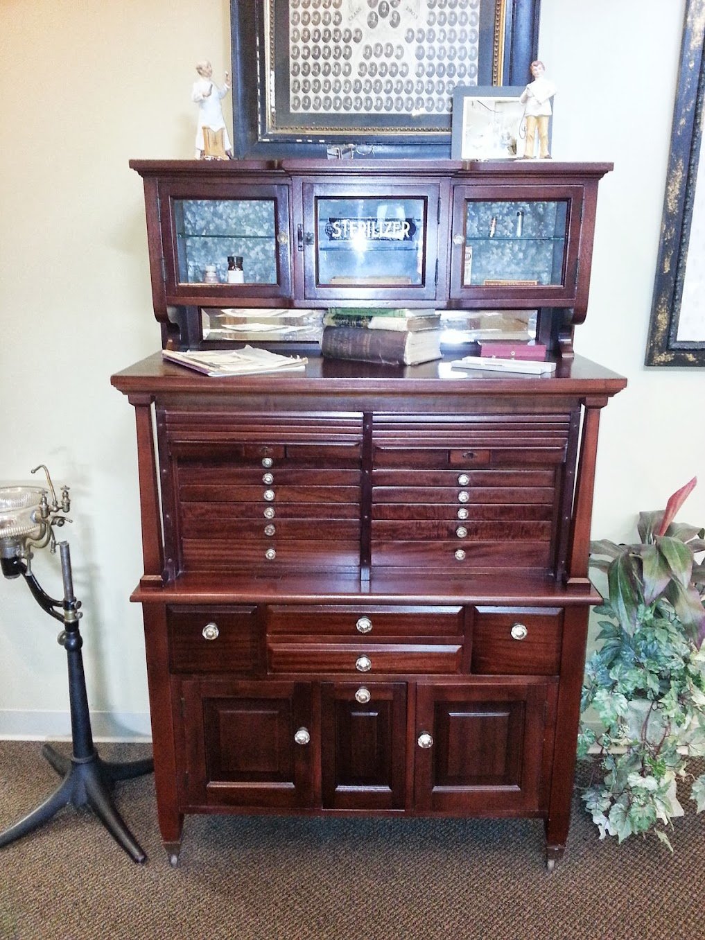 Antique dentist cabinet refinished in rich mahogany by Doll Furniture Company — original etched 'STERILIZER' glass and instrument drawers preserved, now on display at a dental office in Bloomington, Illinois