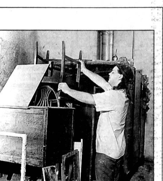 Black and white photograph from The Pantagraph, July 25, 1994 — Jeff Shutt loading wooden chair frames into the Strip-o-lator furniture stripping machine that his grandfather Andrew E. Shutt built by hand in 1969 at Doll Furniture Company in Normal, Illinois