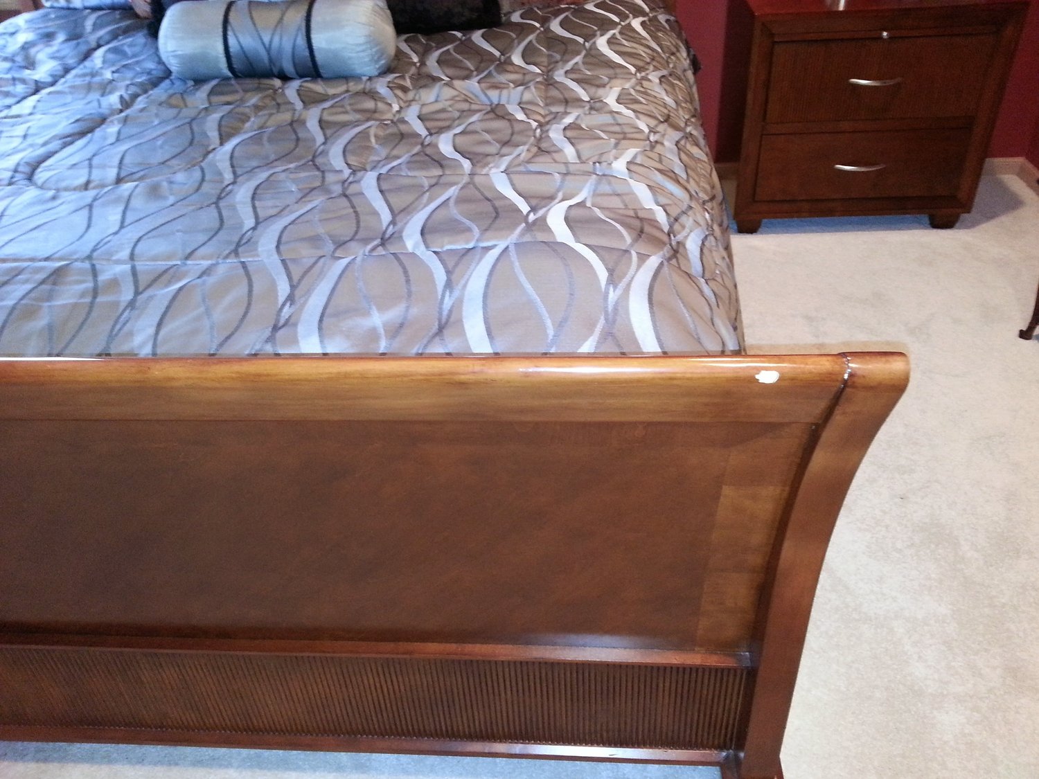 Cherry sleigh bed footboard with a visible white reflection and finish damage on the upper right curve — before furniture finish touchup repair at Doll Furniture Company
