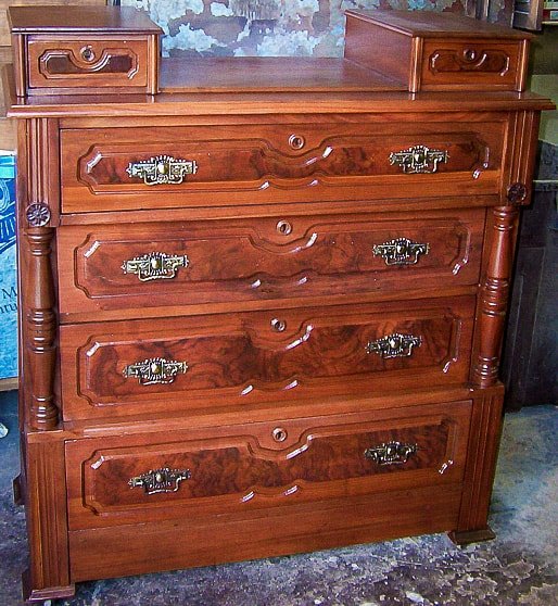 Antique Victorian Eastlake-style walnut dresser refinished by Doll Furniture Company — bookmatched burl walnut drawer panels, fluted half-columns, original engraved brass drop pulls, and two carved glove boxes on top, fully restored to a rich warm finish